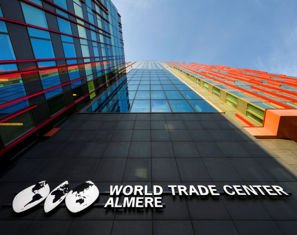 Hoog gebouw van het World Trade Center Almere met kleurrijke glazen gevels vanaf een laag standpunt gefotografeerd.